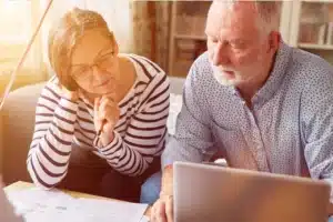 Older couple reviewing retirement paperwork beside a laptop at home