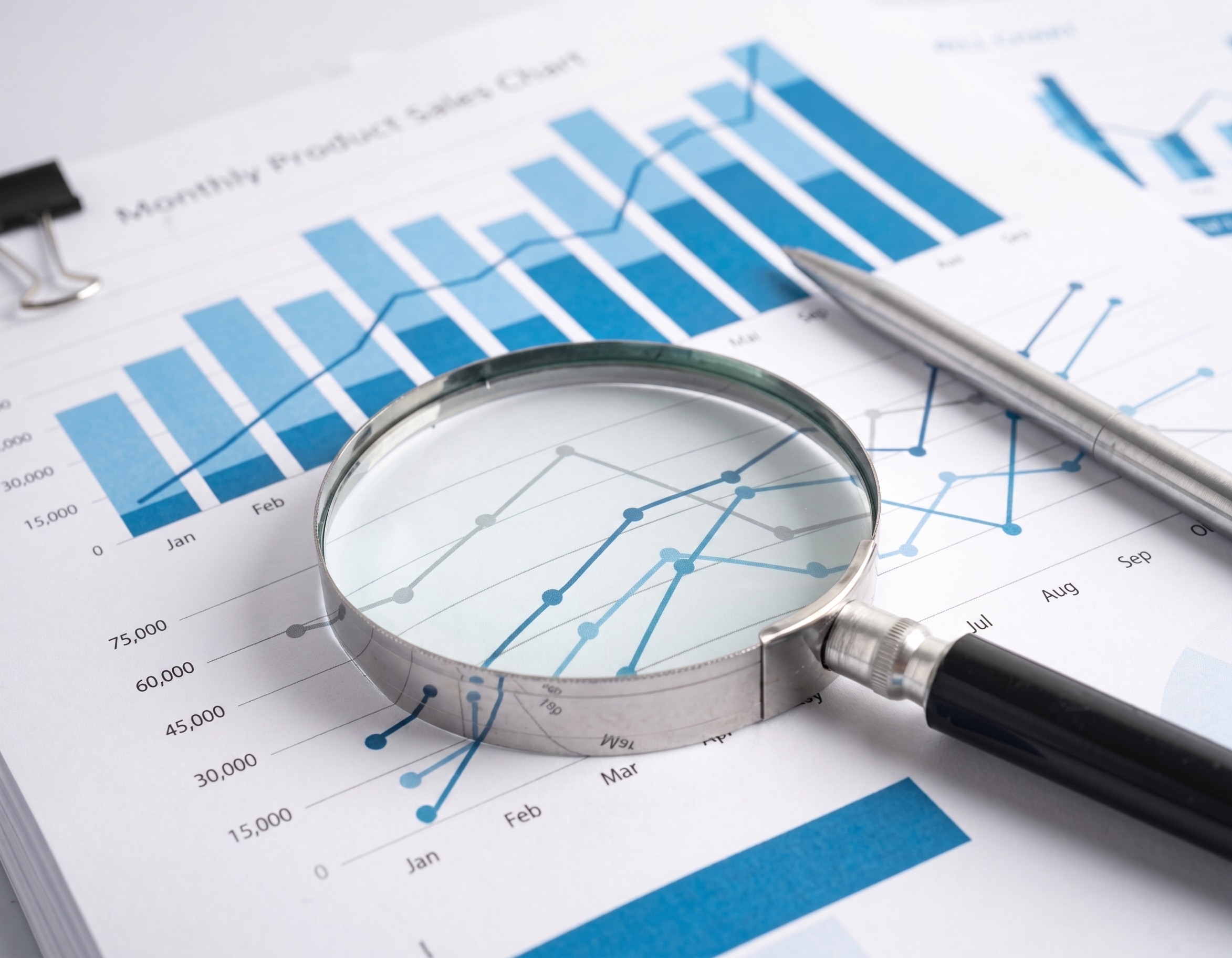 Magnifying glass resting on a sales chart during financial planning for business owners.