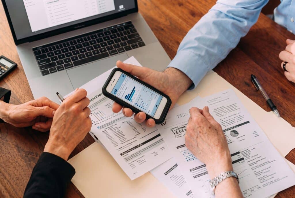 Advisor reviewing charts on a smartphone and paperwork during retirement planning with Lazenby's financial services Leeds.